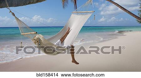 Picture - Caucasian woman laying in hammock on tropical beach. Fotosearch