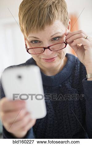 Caucasian woman peering over eyeglasses at cell phone View Large Photo Image Stock Photo - Caucasian woman peering over eyeglasses at cell phone. Fotosearch