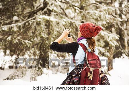 Stock Image - Caucasian woman photographing nature on snowy path. Fotosearch