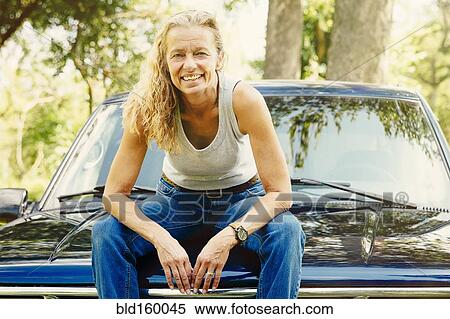 Stock Photography - Caucasian woman sitting on car hood. Fotosearch