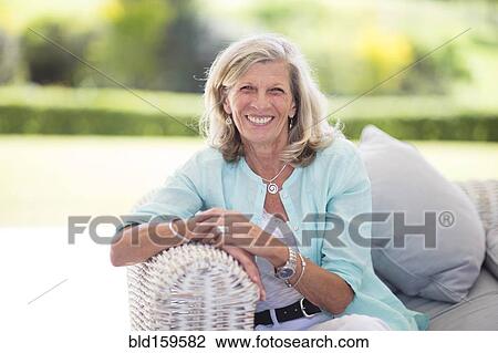 Stock Image - Caucasian woman sitting on sofa outdoors. Fotosearch