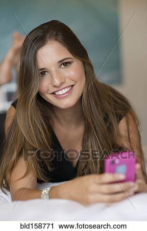 Stock Image - Caucasian woman using cell phone on bed. Fotosearch