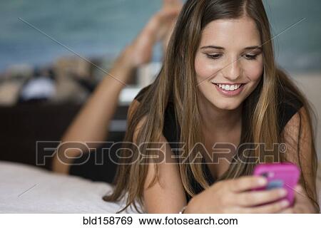 Stock Photo - Caucasian woman using cell phone on bed. Fotosearch