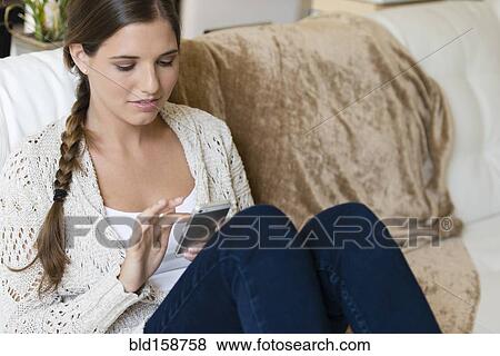 Stock Photo - Caucasian woman using cell phone on sofa. Fotosearch