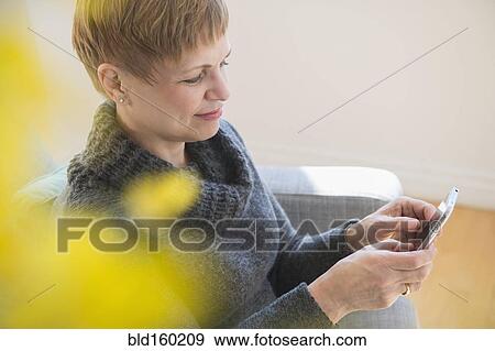 Stock Photo - Caucasian woman using cell phone on sofa. Fotosearch