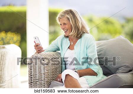 Stock Image - Caucasian woman using cell phone on sofa outdoors. Fotosearch