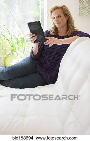 Picture - Caucasian woman using digital tablet on sofa. Fotosearch