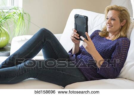 Stock Photograph - Caucasian woman using digital tablet on sofa. Fotosearch
