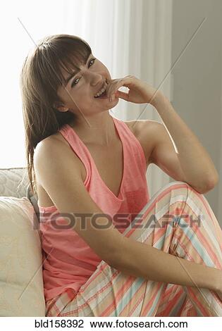 Stock Image - Caucasian woman wearing pajamas smiling on sofa. Fotosearch