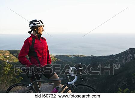 Stock Image - Caucasian woman with bicycle admiring scenic view of mountains. Fotosearch