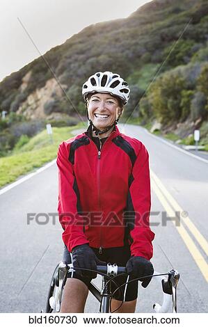 Stock Image - Caucasian woman with bicycle smiling on remote mountain road. Fotosearch