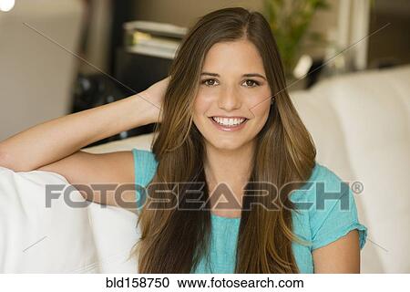 Stock Image - Caucasian woman with long hair sitting on sofa. Fotosearch
