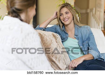 Stock Image - Caucasian women talking on sofa. Fotosearch