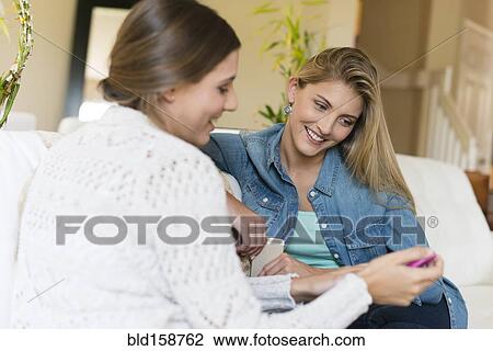 Stock Image - Caucasian women using cell phone on sofa. Fotosearch
