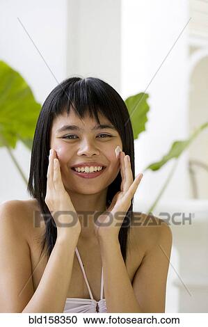 Stock Image - Chinese woman applying moisturizer on face. Fotosearch
