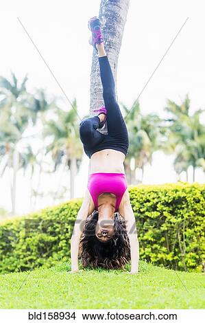 Picture - Chinese woman doing handstand against tree in park. Fotosearch