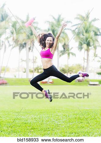 Stock Image - Chinese woman jumping for joy in park. Fotosearch
