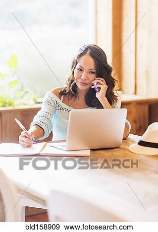 Stock Photo - Chinese woman on cell phone using laptop in cafe. Fotosearch