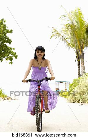 Stock Image - Chinese woman riding bicycle on tropical beach. Fotosearch