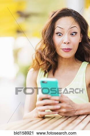 Stock Image - Chinese woman using cell phone at sidewalk cafe. Fotosearch