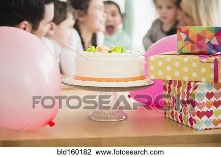 Stock Image - Close up of birthday cake, wrapped gifts and balloon at party. Fotosearch