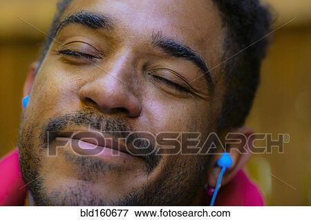 Stock Photo - Close up of calm mixed race man listening to earbud. Fotosearch