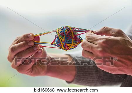 Stock Photo - Close up of Caucasian man pulling rubber band ball. Fotosearch