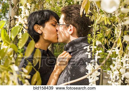 Stock Photo - Close up of couple kissing in foliage. Fotosearch