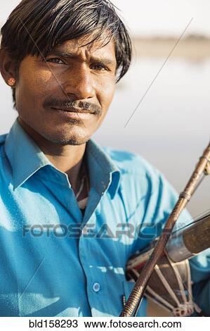 Stock Image - Close up of Indian man holding traditional instrument. Fotosearch