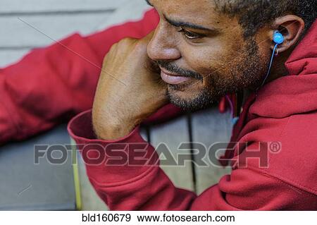 Stock Photo - Close up of mixed race man listening to earbud. Fotosearch
