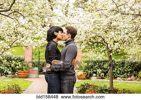 Stock Photo - Couple kissing under flowering trees in park. Fotosearch