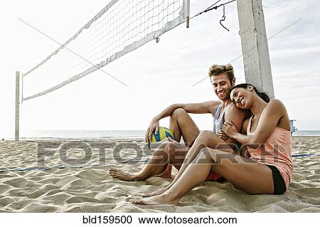Stock Image - Couple sitting near volleyball net on beach. Fotosearch