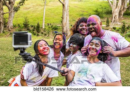 Stock Photograph - Friends covered in pigment powder using selfie stick. Fotosearch
