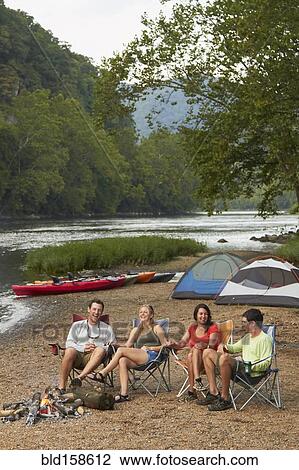 Stock Image - Friends relaxing around campfire at campsite. Fotosearch