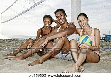 Stock Image - Friends sitting near volleyball net on beach. Fotosearch