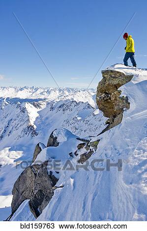 Stock Image - Hiker admiring scenic view from snowy mountaintop. Fotosearch