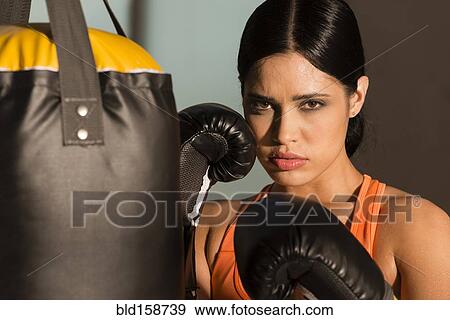 Stock Photo - Hispanic boxer standing near punching bag in gymnasium. Fotosearch