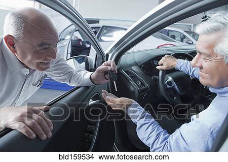 Picture - Hispanic car salesman handing keys to customer. Fotosearch