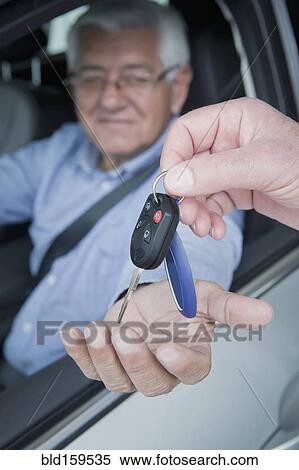 Stock Photography - Hispanic car salesman handing keys to customer. Fotosearch