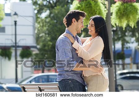Stock Image - Hispanic couple hugging in urban park. Fotosearch
