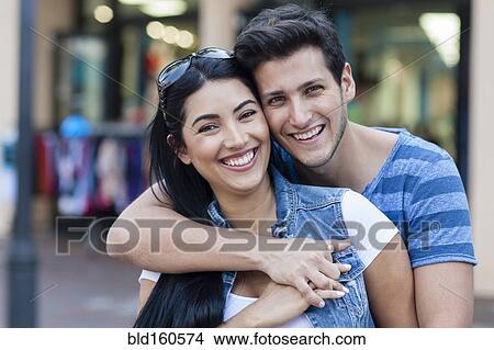 Picture - Hispanic couple hugging on city sidewalk. Fotosearch