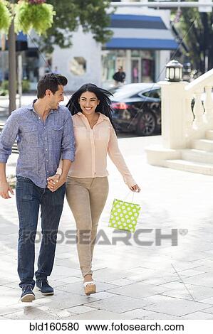 Stock Image - Hispanic couple walking on city sidewalk. Fotosearch
