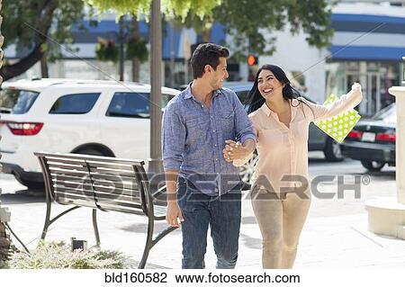 Stock Image - Hispanic couple walking on city sidewalk. Fotosearch