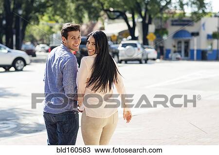 Stock Image - Hispanic couple walking on city sidewalk. Fotosearch