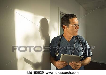 Stock Photo - Hispanic doctor leaning on wall using digital tablet. Fotosearch