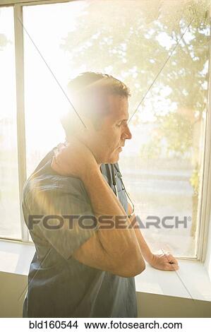 Picture - Hispanic doctor rubbing his neck near window. Fotosearch
