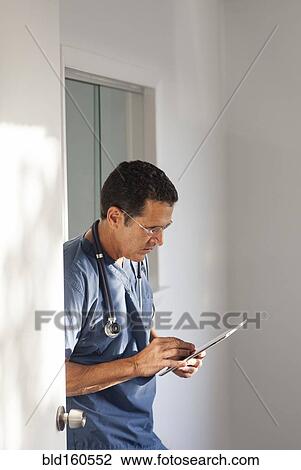 Stock Image - Hispanic doctor using digital tablet in hallway. Fotosearch