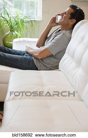Stock Image - Hispanic man talking on cell phone on sofa. Fotosearch