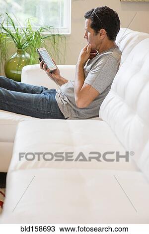 Stock Image - Hispanic man using cell phone on sofa. Fotosearch