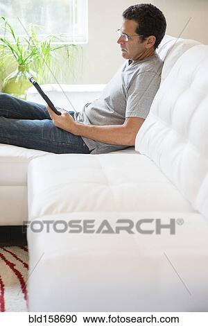 Stock Image - Hispanic man using digital tablet on sofa. Fotosearch
